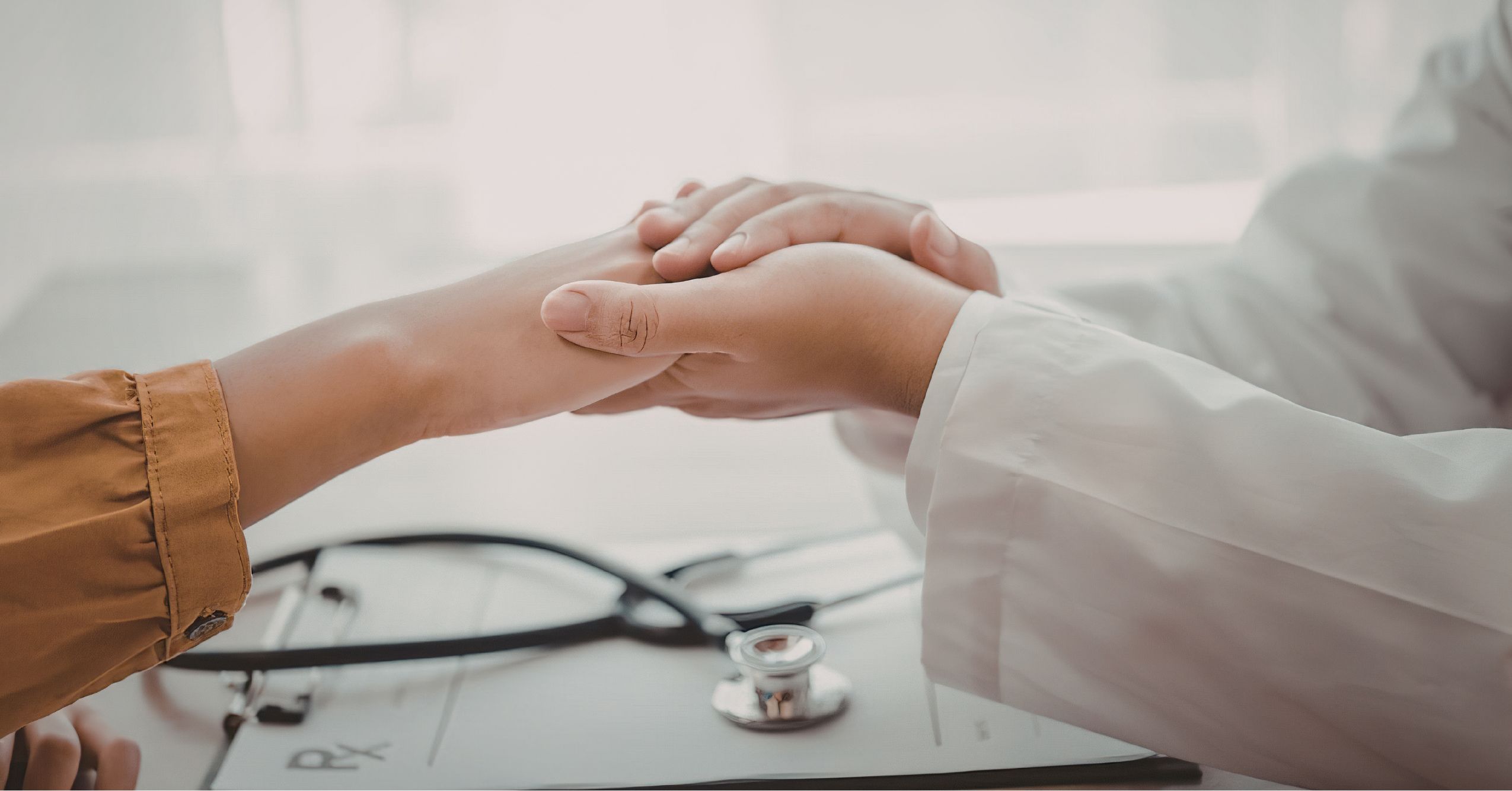 Clinical Integrity in Healthcare Documentation A close-up of a doctor in a white lab coat holding a patient's hand in a comforting gesture over a medical chart and stethoscope.