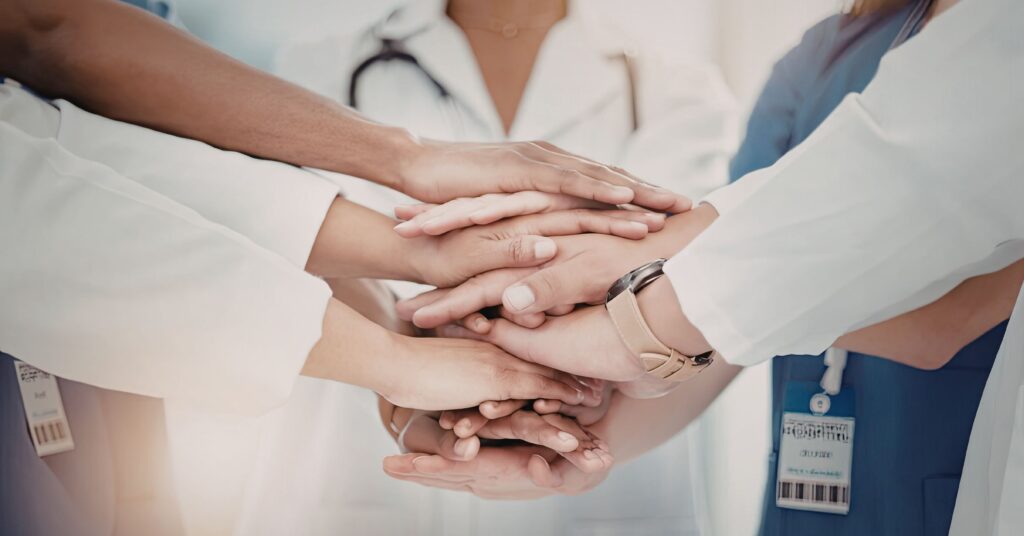Integrated Healthcare Coding and Clinical Support | ASAAR Medical A diverse team of healthcare professionals in white lab coats and blue scrubs placing their hands together in a stack, symbolizing the unified support between clinical staff and medical coding specialists.